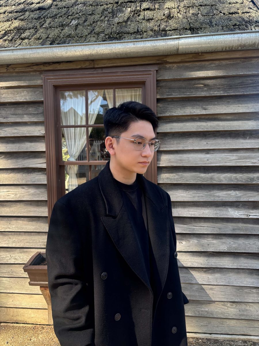 Portrait of Quan in a black coat in front of a weathered timber cottage